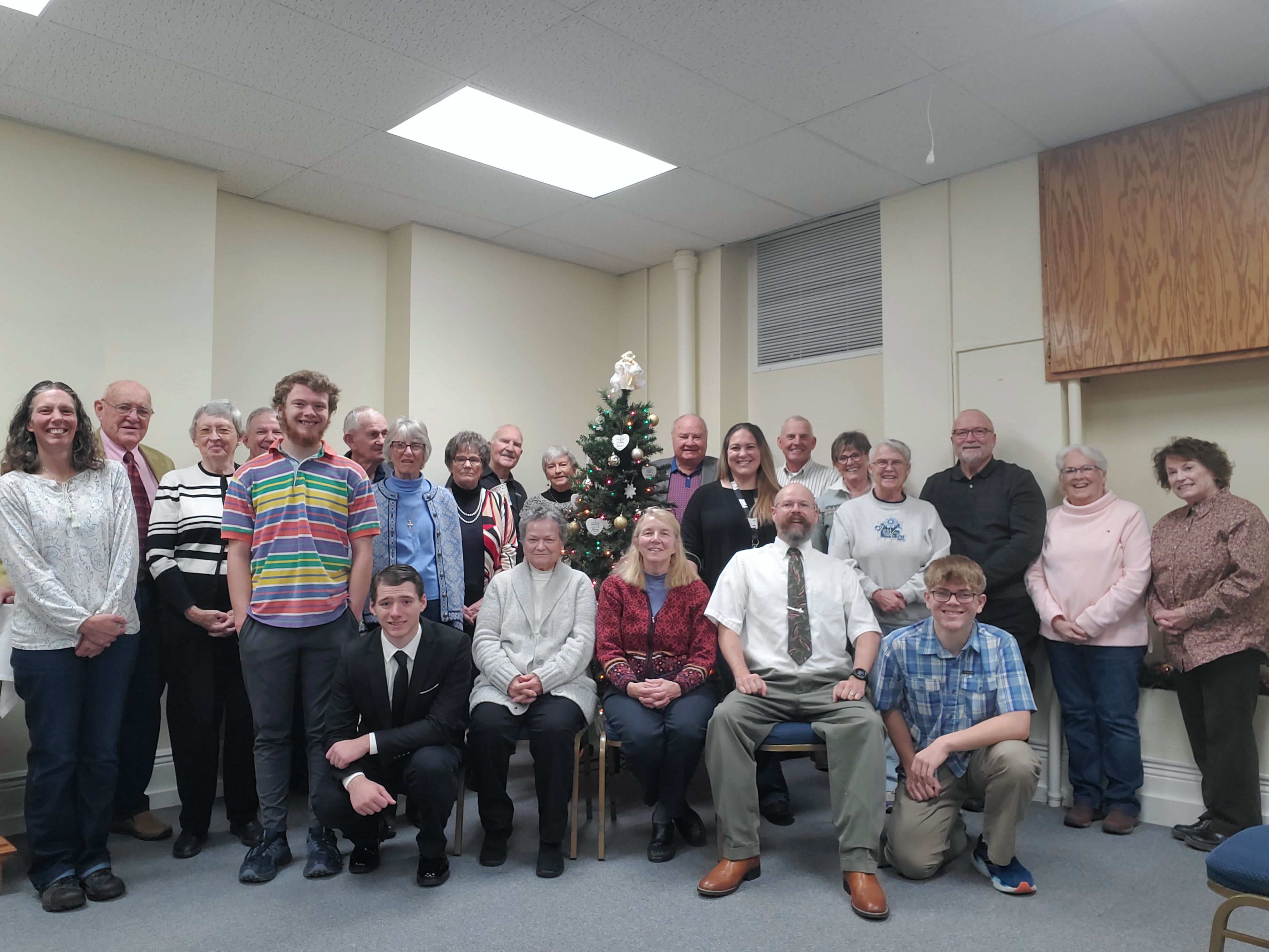 Pastor and members of Christ the King posing for a Christmas picture in front of a Christmas tree